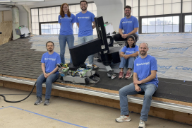 Six people are sitting on top of a roof display with a roof robot between them.