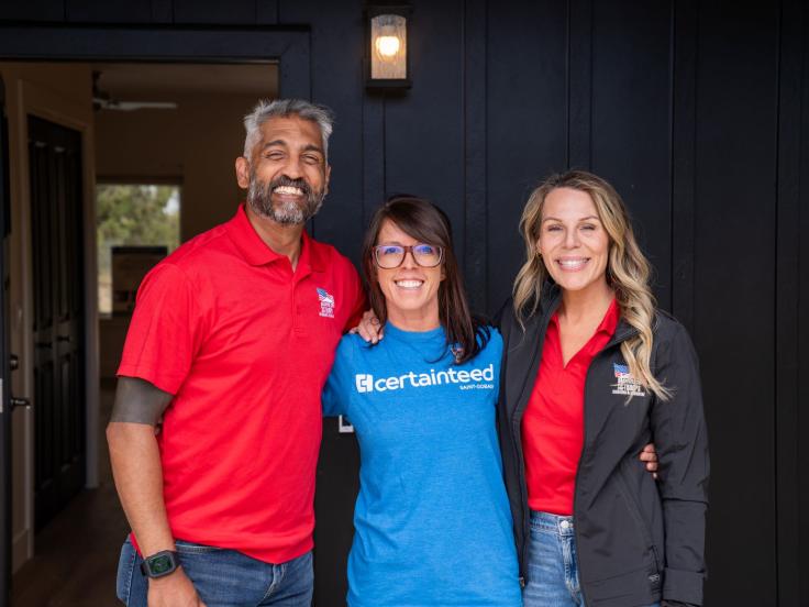 A man wearing a red shirt and his wife, also wearing a white shirt, pose with a CertainTeed employee in front of their new home