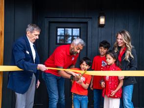 A family wearing red is cutting the yellow ribbon in front of their new home