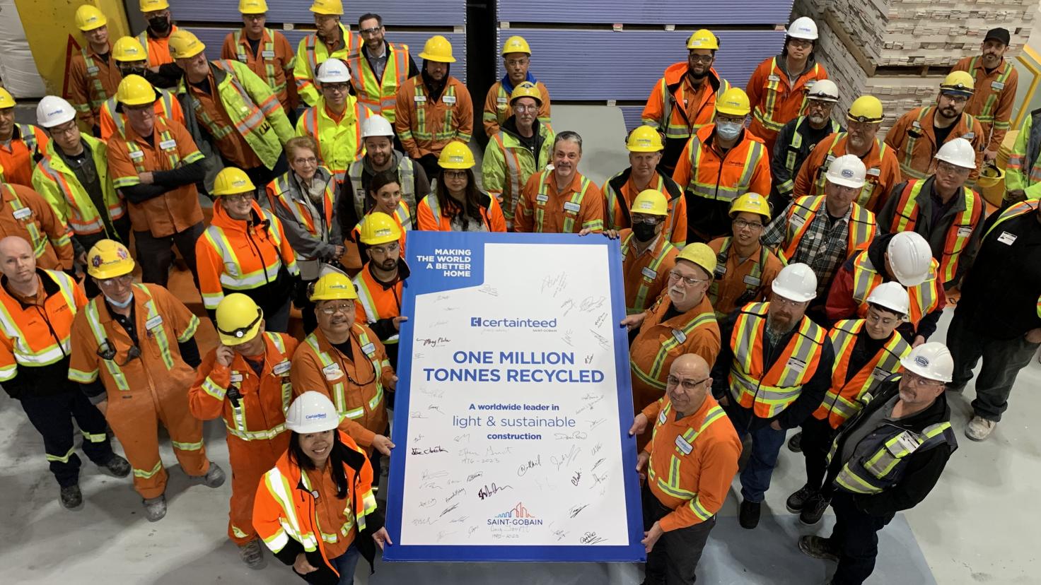 A large group of people in safety vets and hard hats gather around a sign that says One Million Tonnes Recycled