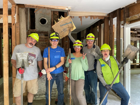 Five people with hard hats pose inside a house under construction