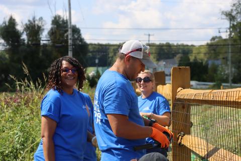 Three people are building a fence wearing matching blue shirts